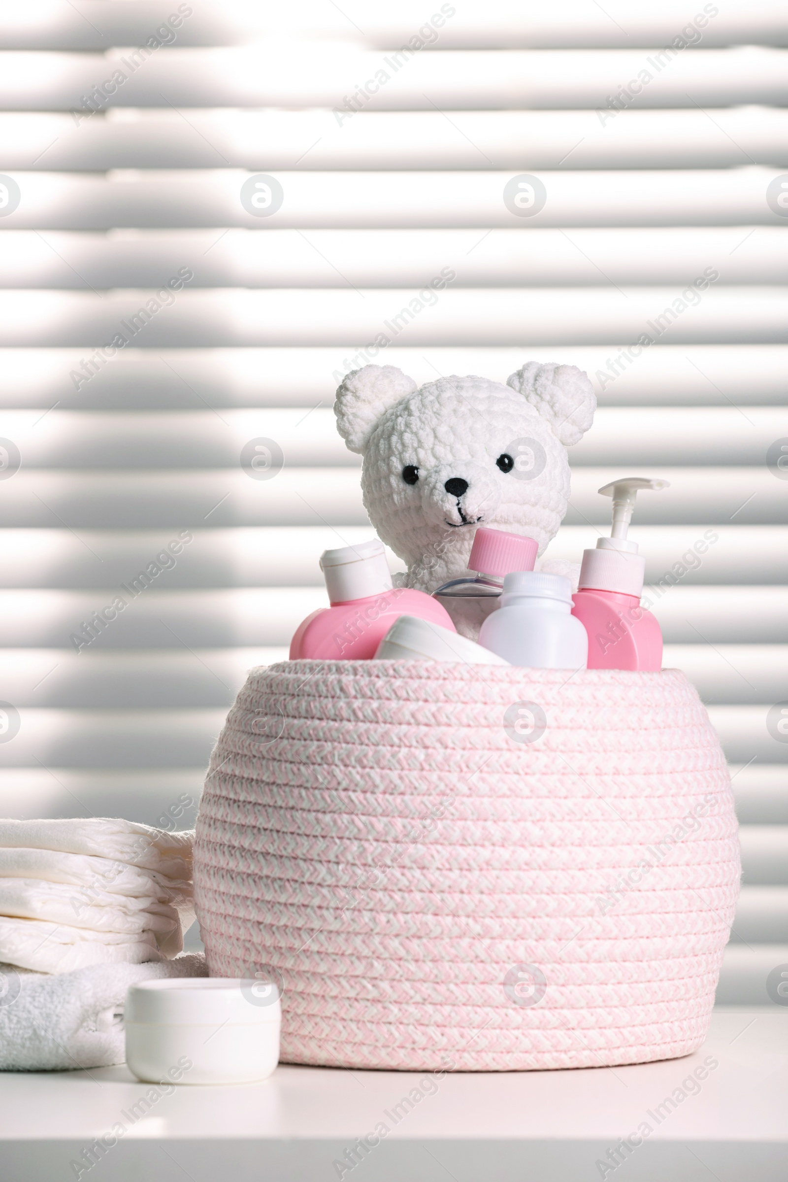 Photo of Wicker basket with baby cosmetic products and knitted toy bear on white table