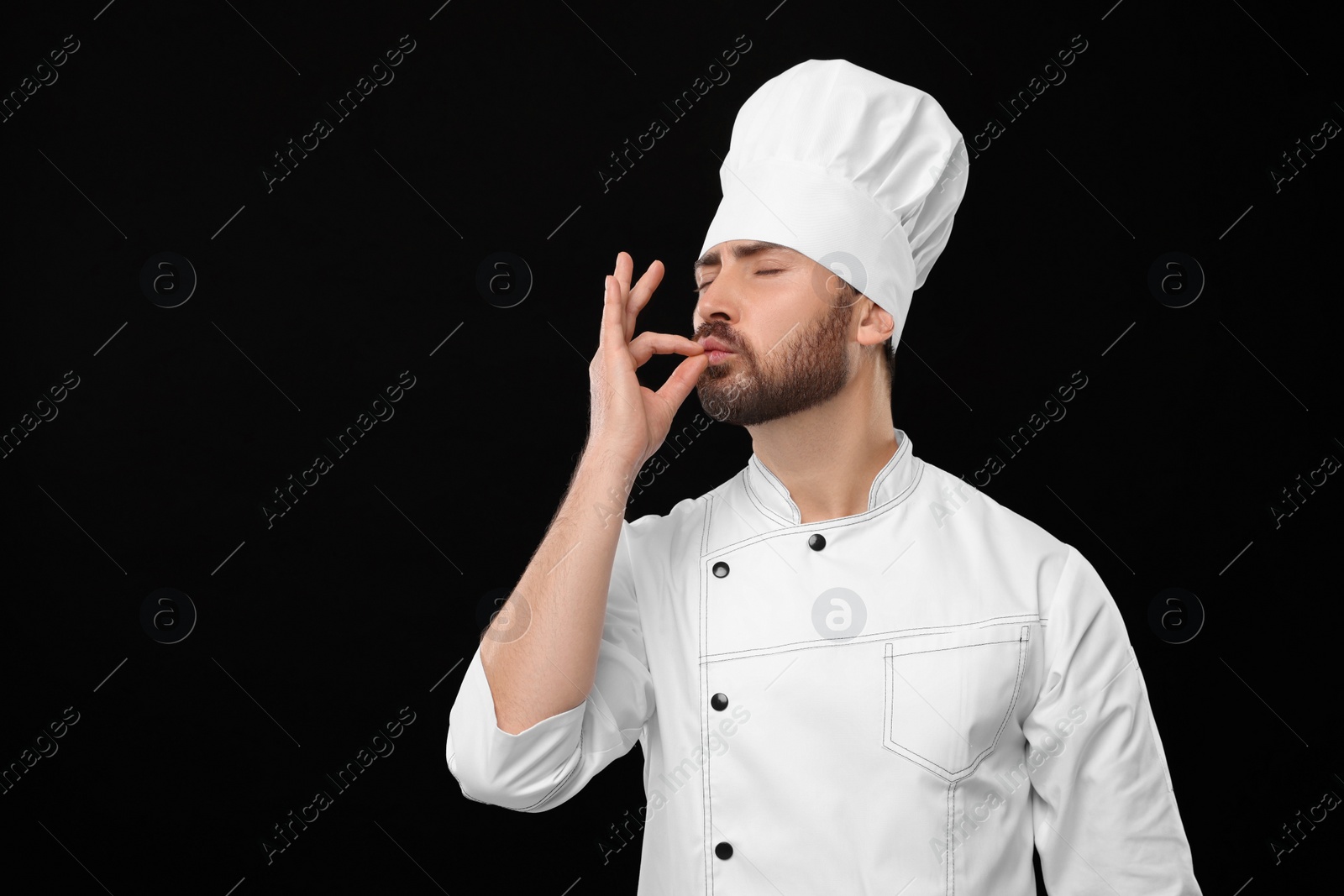 Photo of Mature chef showing delicious gesture on black background, space for text