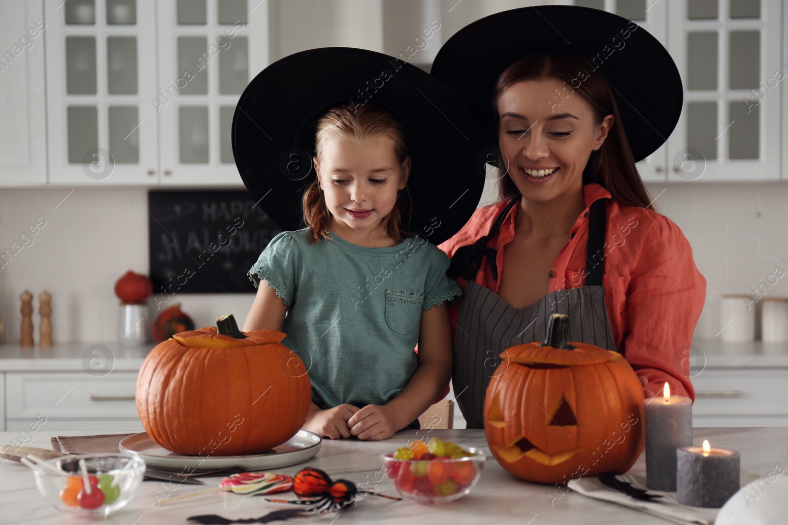 Photo of Mother and daughter making pumpkin jack o'lanterns at table in kitchen. Halloween celebration