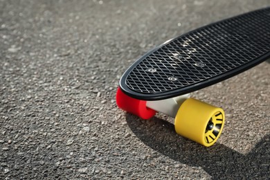 Black skateboard with colorful wheels on asphalt outdoors, closeup