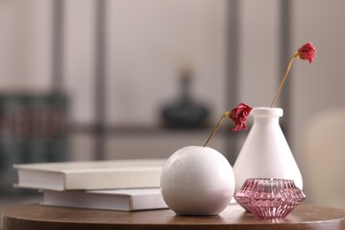 Photo of Vases with dried flowers, candle and books on wooden table in room, space for text