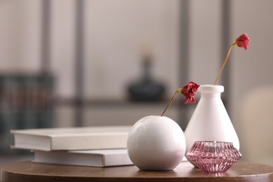 Vases with dried flowers, candle and books on wooden table in room, space for text