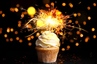 Delicious birthday cupcake with sparkler on black table against blurred lights