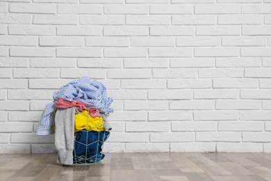 Photo of Laundry basket with dirty clothes on floor near brick wall. Space for text