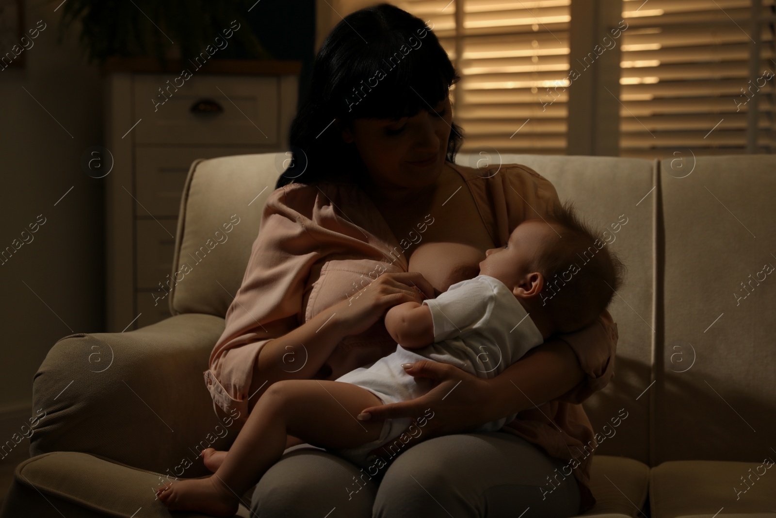 Photo of Woman breastfeeding her little baby on sofa in evening