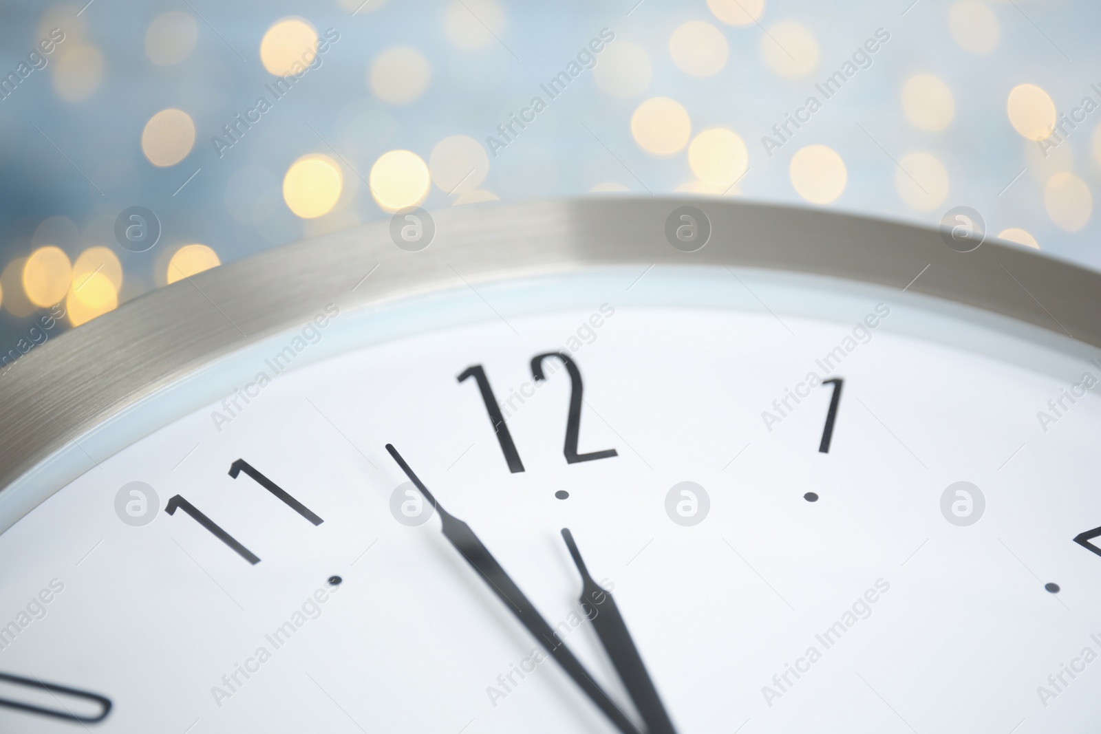 Photo of Clock on light blue background with blurred lights, closeup. New Year countdown