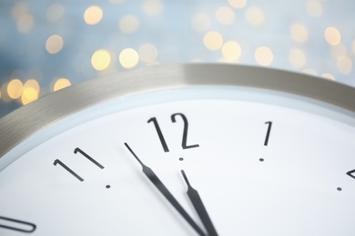 Photo of Clock on light blue background with blurred lights, closeup. New Year countdown