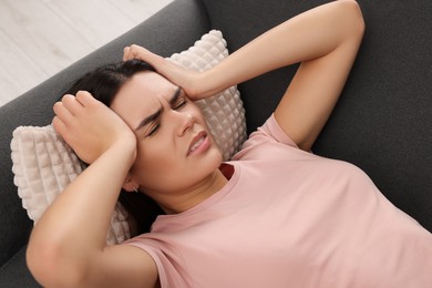 Photo of Sad woman suffering from headache on sofa indoors
