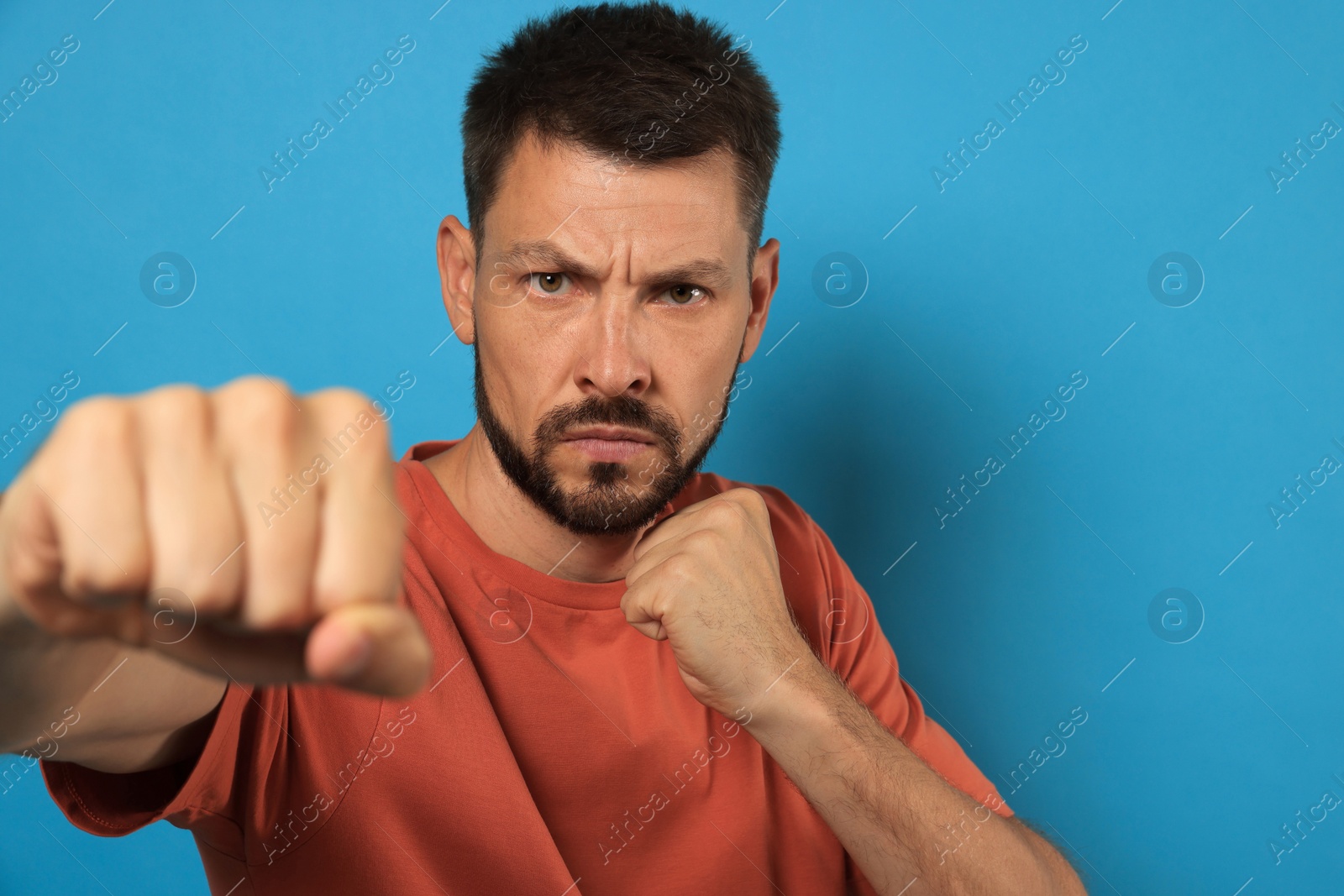 Photo of Man throwing punch on light blue background. Space for text