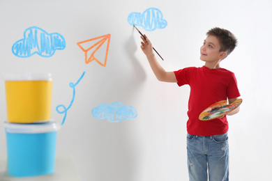 Little child drawing paper plane and sky on white wall indoors