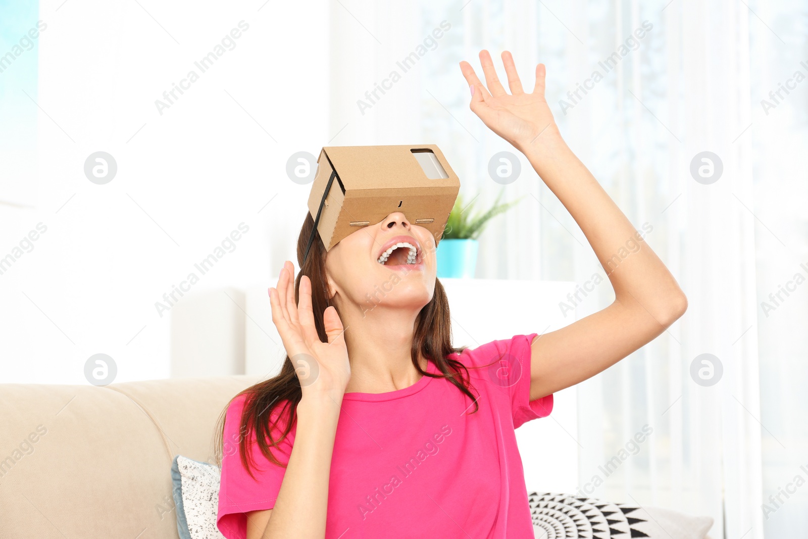 Photo of Young woman using cardboard virtual reality headset at home