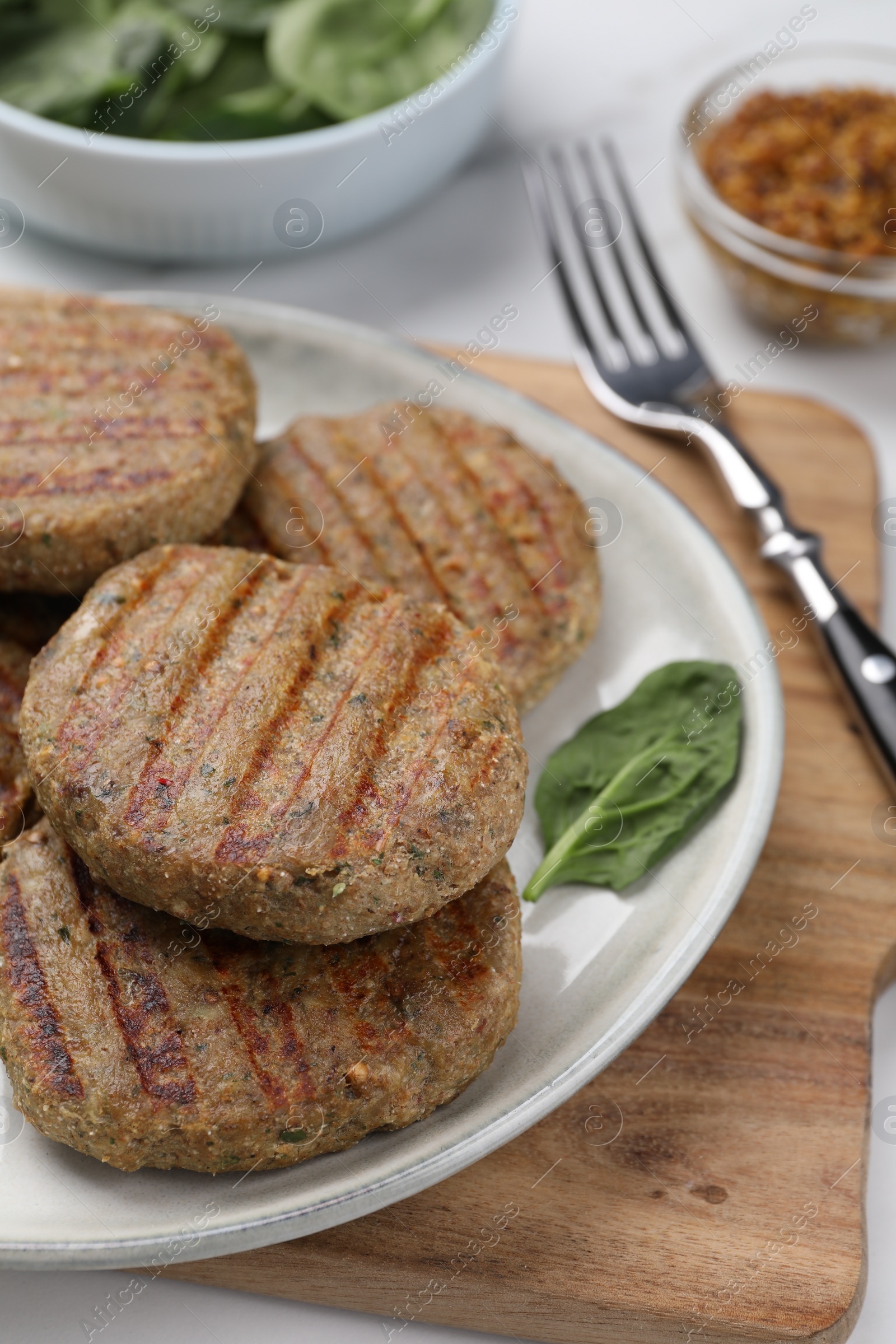 Photo of Tasty grilled vegan cutlets and spinach on wooden board, closeup