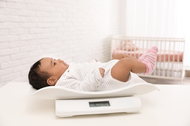 African-American baby lying on scales in light room