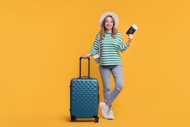 Happy young woman with passport, ticket and suitcase on yellow background