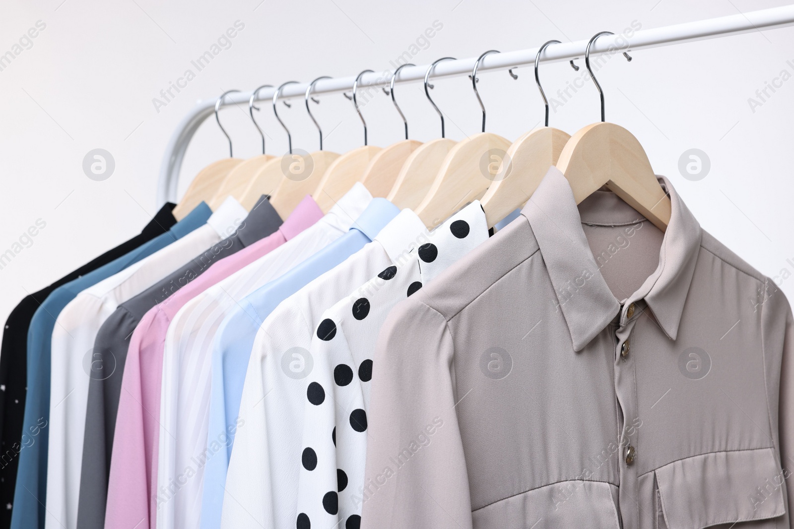 Photo of Dry-cleaning service. Many different clothes hanging on rack against white background, closeup