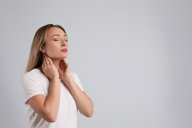 Photo of Young woman doing thyroid self examination on light grey background, space for text