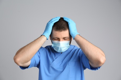 Photo of Stressed doctor in protective mask on grey background. Mental health problems during COVID-19 pandemic