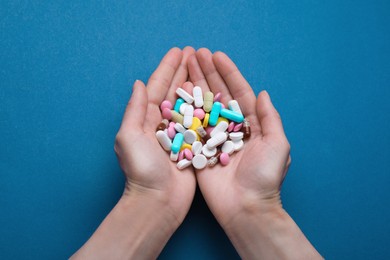 Photo of Woman holding colorful antidepressants on blue background, top view