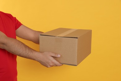 Photo of Courier holding cardboard box on yellow background, closeup