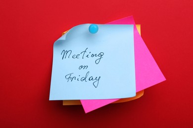 Photo of Paper note with words Meeting on Friday pinned to red background