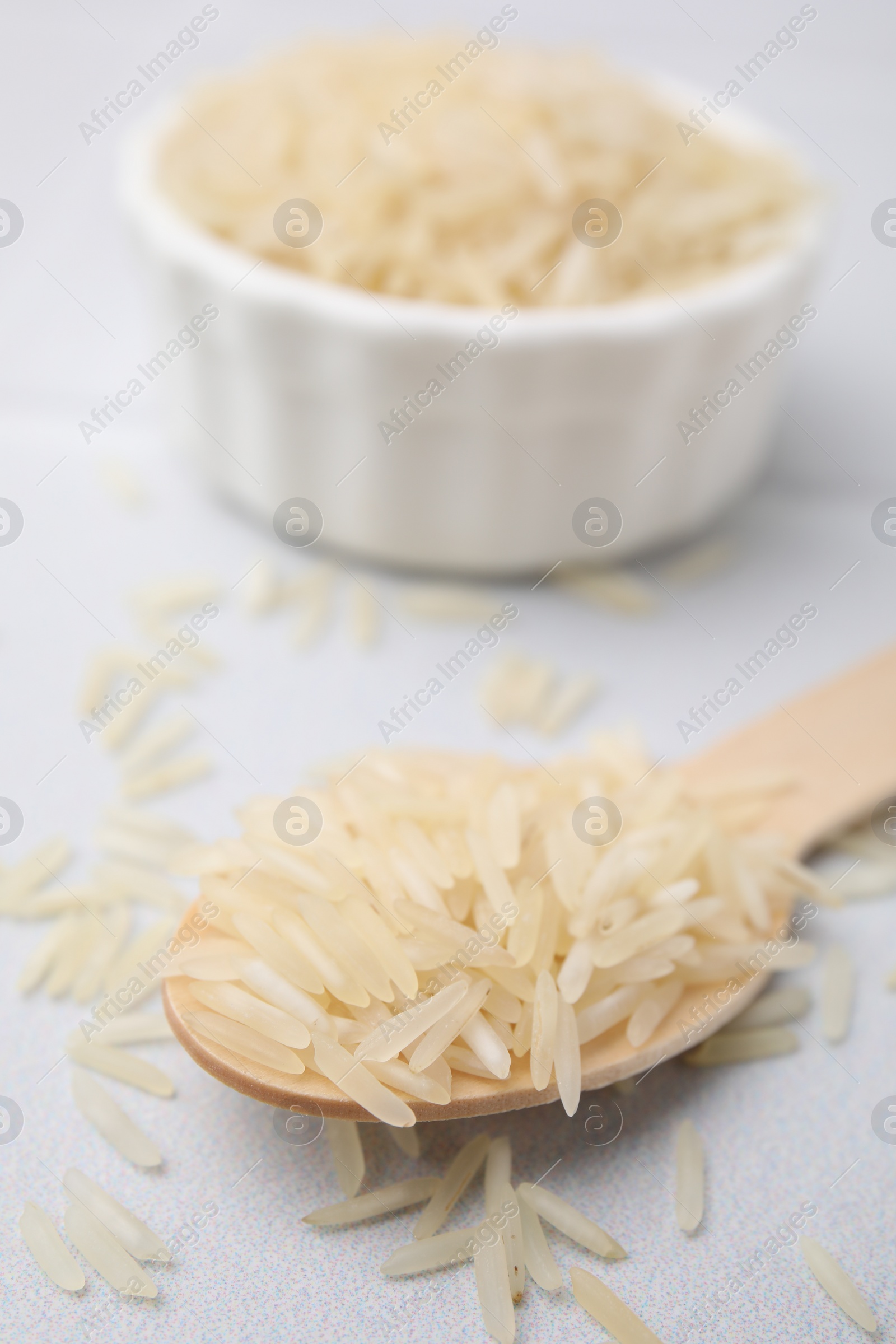 Photo of Wooden spoon with raw rice on white table, closeup