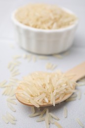 Wooden spoon with raw rice on white table, closeup