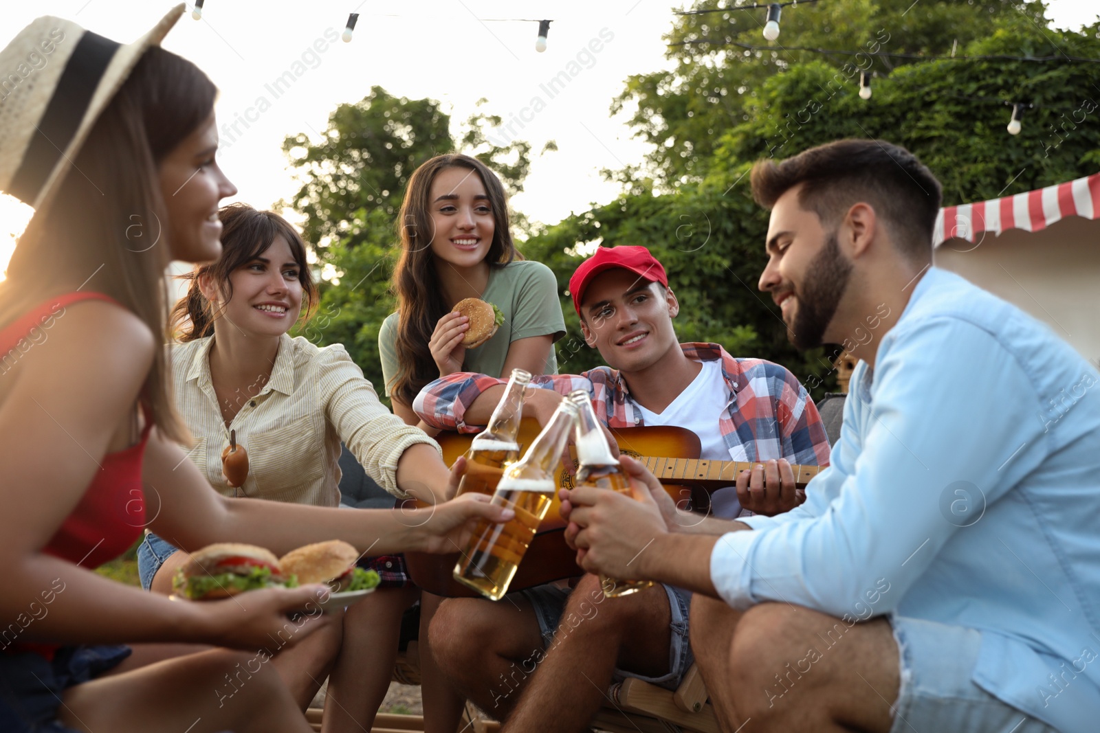 Photo of Happy friends with food and beer resting near motorhome. Camping season