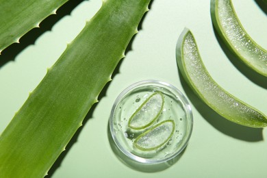 Photo of Cut aloe vera leaves and cosmetic gel on light green background, flat lay