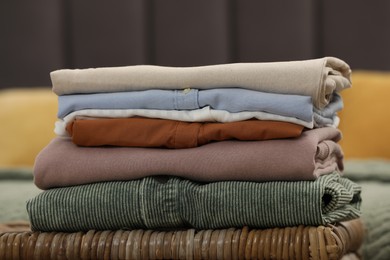 Photo of Sorting and organizing. Stack of different folded clothes on wicker table indoors, closeup