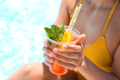Woman with glass of refreshing drink near swimming pool, closeup