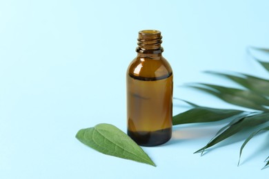 Photo of Bottle of cosmetic oil and leaves on light blue background, closeup