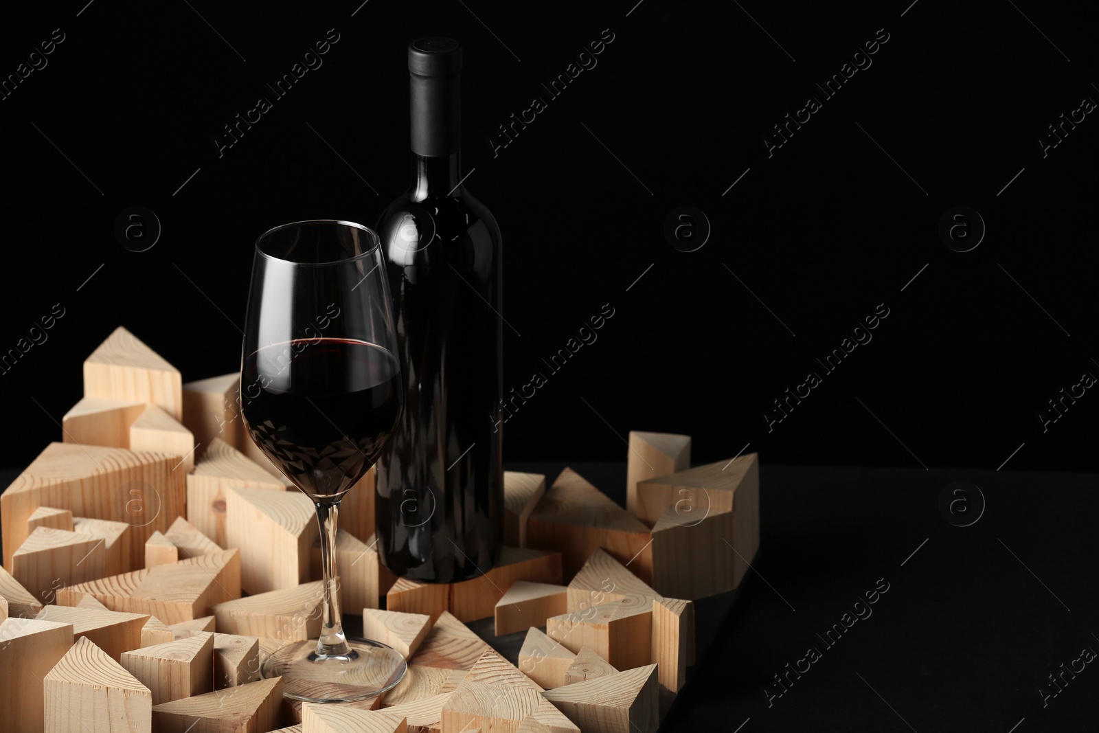 Photo of Stylish presentation of red wine in bottle and wineglass on black background, space for text