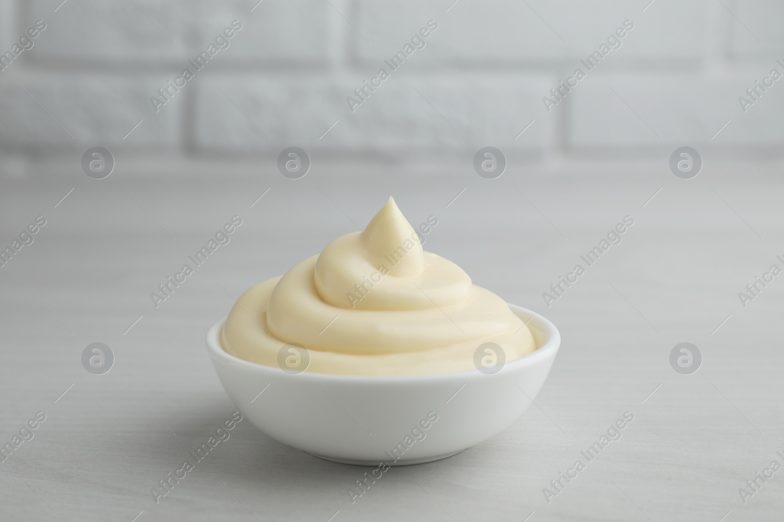 Photo of Tasty mayonnaise sauce in bowl on light wooden table, closeup