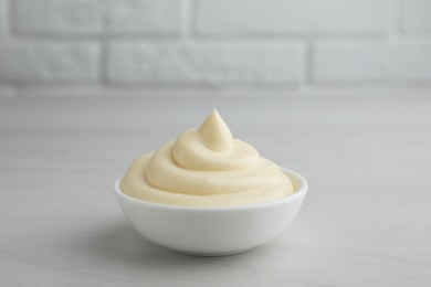 Photo of Tasty mayonnaise sauce in bowl on light wooden table, closeup