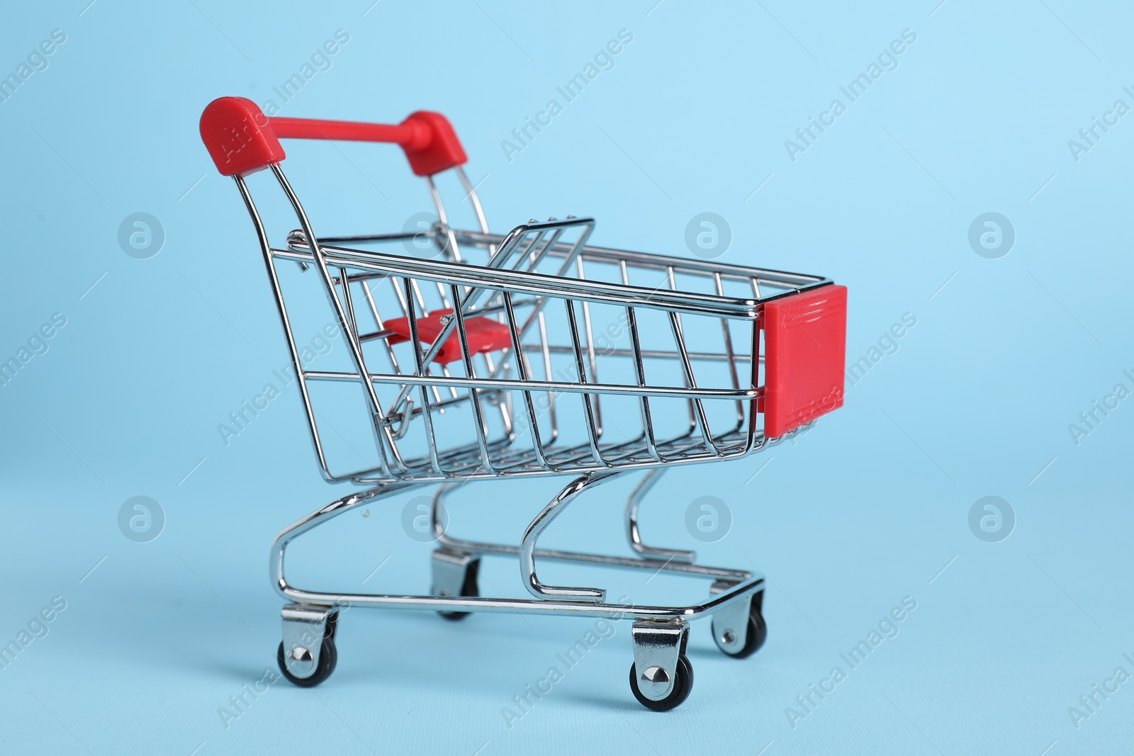 Photo of Small metal shopping cart on light blue background