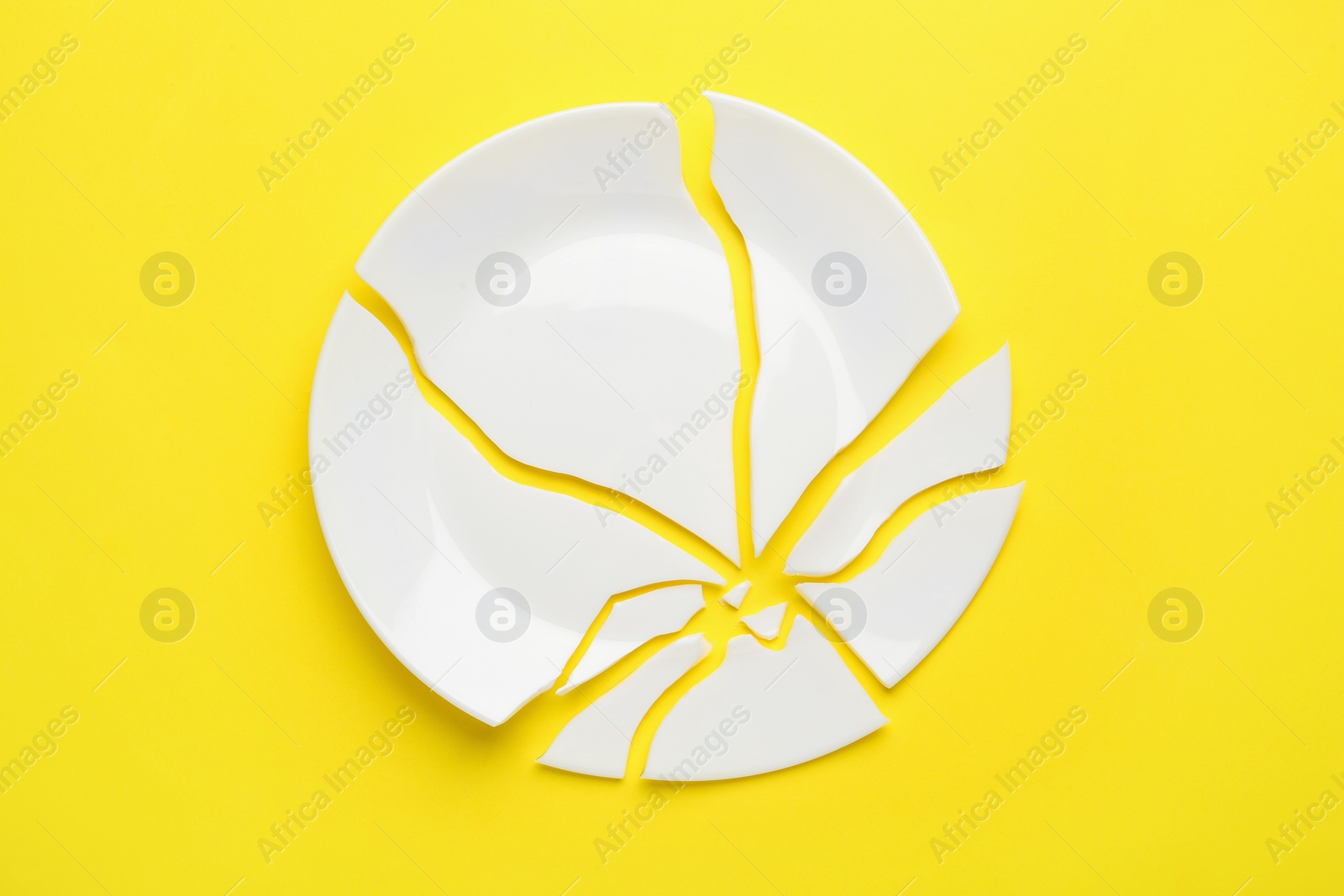 Photo of Pieces of broken ceramic plate on yellow background, flat lay