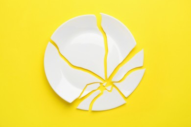 Pieces of broken ceramic plate on yellow background, flat lay