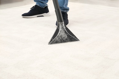 Man removing dirt from carpet with vacuum cleaner indoors, closeup. Space for text