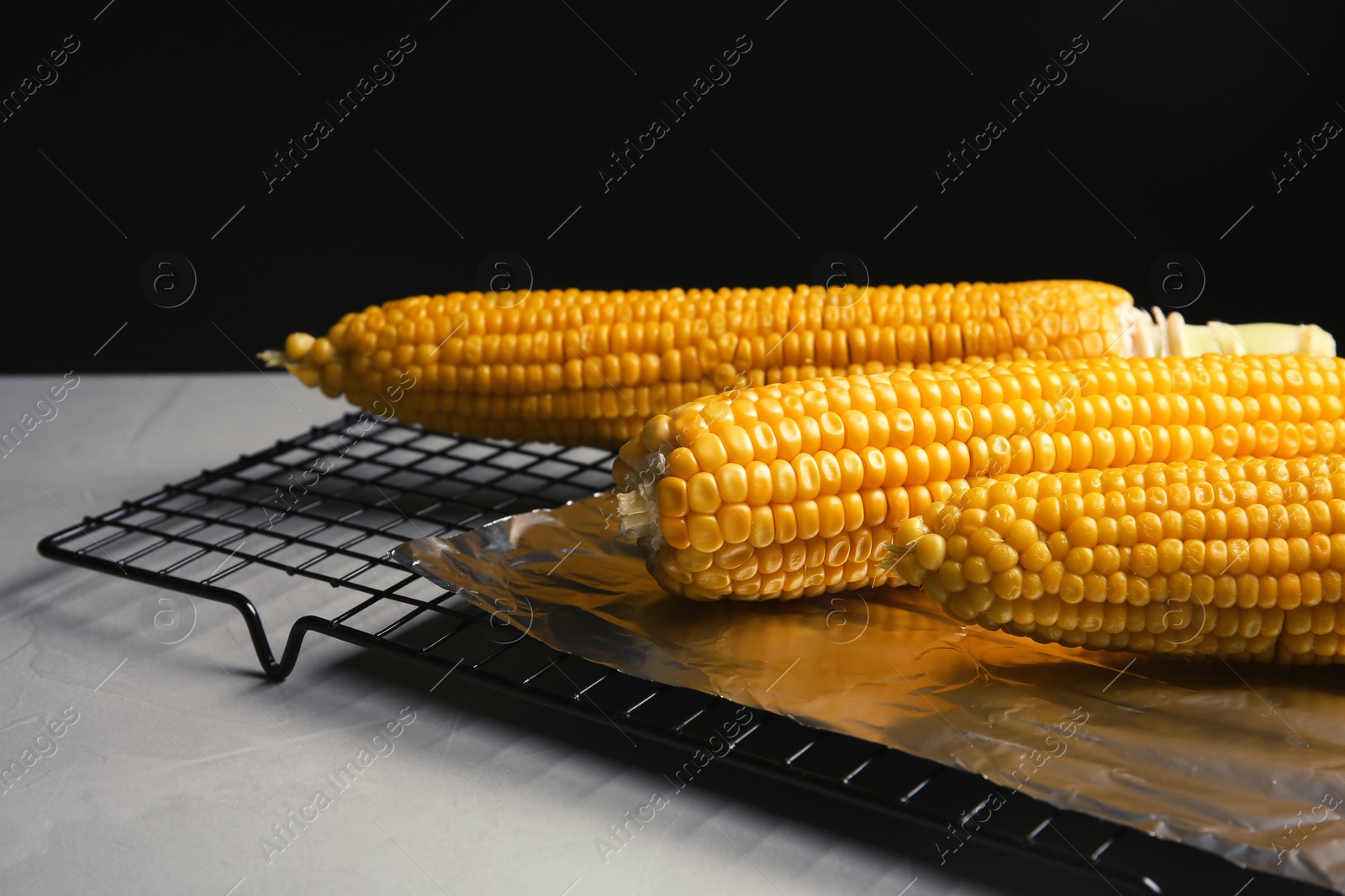 Photo of Baking rack with fresh corn cobs on light table against black background