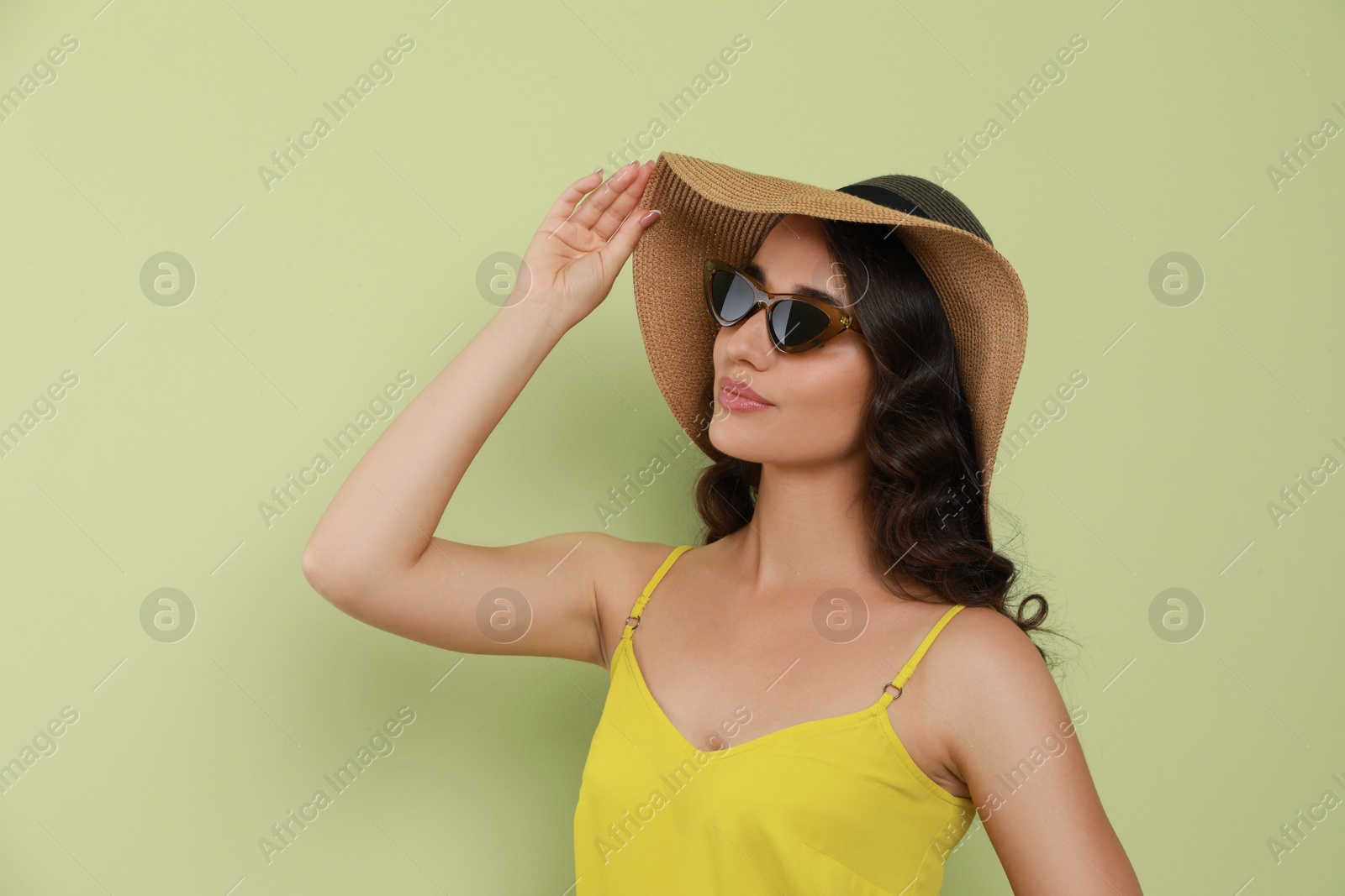 Photo of Beautiful young woman with straw hat and stylish sunglasses on light green background