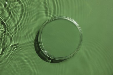 Photo of Stylish presentation for product. Glass podium in water on pale green background, top view