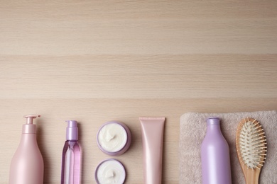 Different hair care products, towel and brush on wooden table, flat lay. Space for text