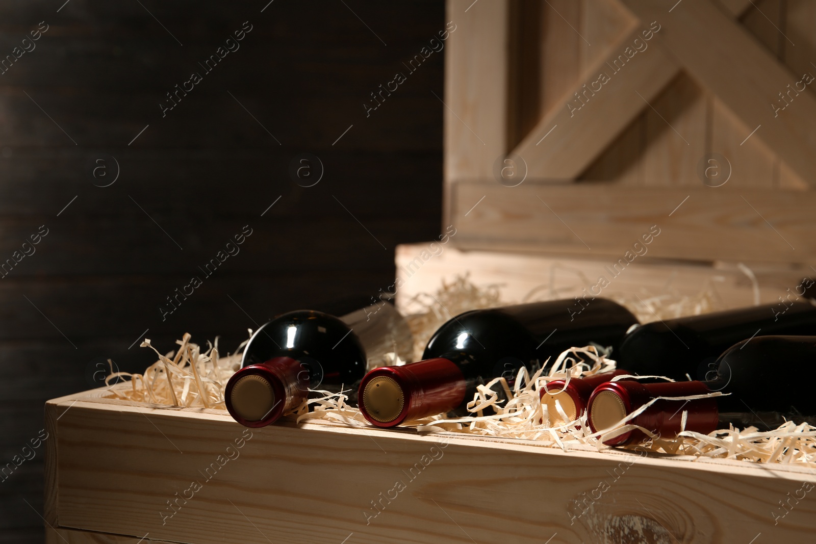 Photo of Wooden crate with bottles of wine on dark background, closeup