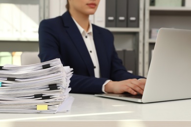 Photo of Female worker working with laptop near stack of documents in office, closeup