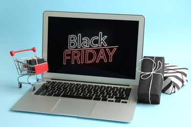 Photo of Laptop with Black Friday announcement, small shopping cart and gifts on light blue background