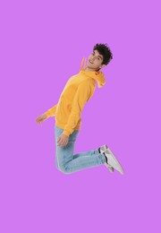 Teenage boy jumping on violet background, full length portrait