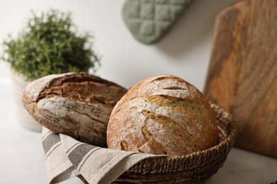 Photo of Wicker bread basket with freshly baked loaves on table in kitchen, closeup