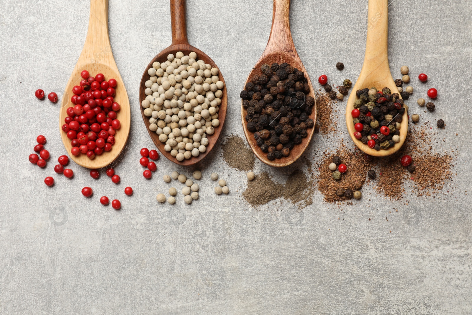 Photo of Aromatic spice. Different peppers in spoons on light textured table, flat lay. Space for text