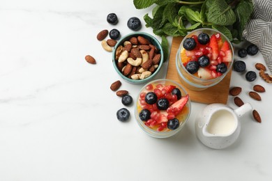 Delicious fruit salad, fresh berries, mint and nuts on white marble table, flat lay. Space for text