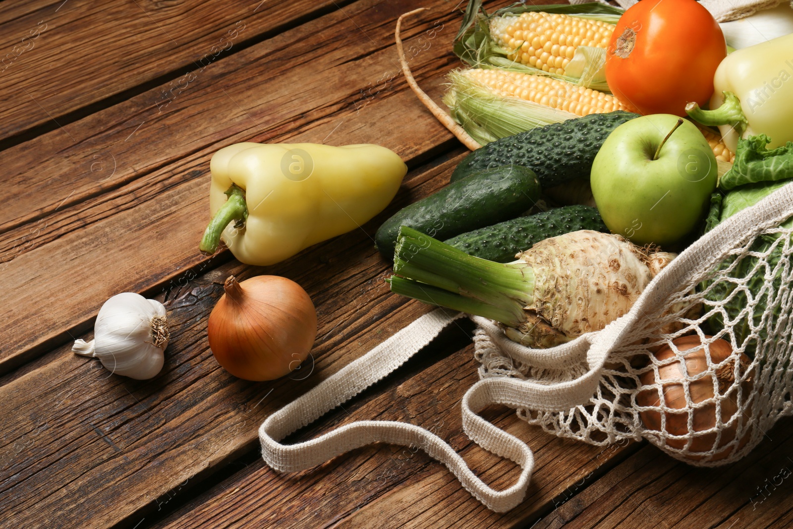 Photo of Different fresh vegetables in net bag on wooden table, closeup. Farmer harvesting